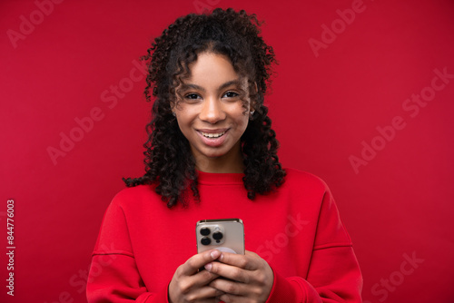 Portrait of a young girl smiling at the camera while standing against a red background. 