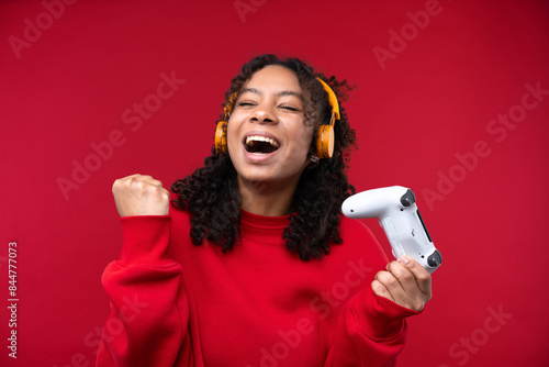 Portrait of a young girl with headphone smiling at the camera while standing against a red background. 