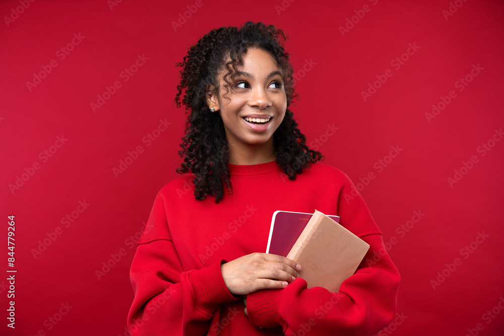 Portrait of a young girl with notebook smiling at the camera while standing against a red background. Portrait of a young girl with notebook smiling at the camera while standing against a red background.