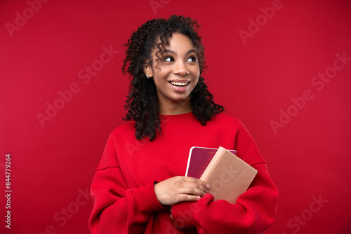 Portrait of a young girl with notebook smiling at the camera while standing against a red background. 