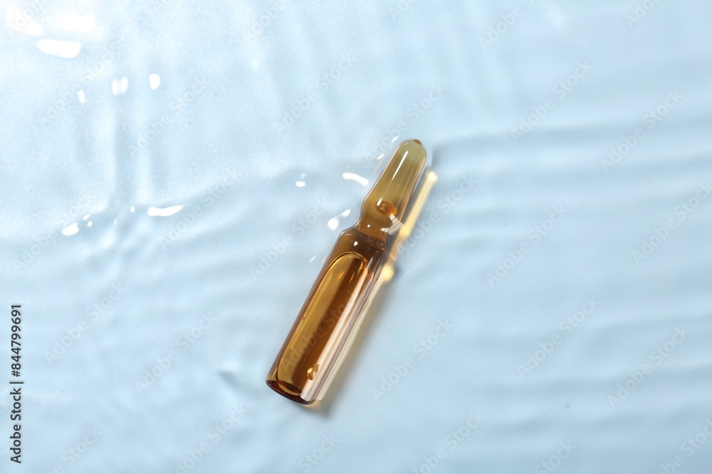 Skincare ampoule in water on light blue background, top view Skincare ampoule in water on light blue background, top view