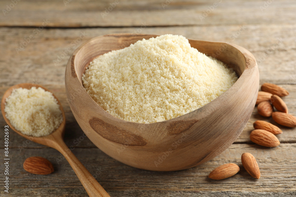 Fresh almond flour in bowl, spoon and nuts on wooden table, closeup Fresh almond flour in bowl, spoon and nuts on wooden table, closeup