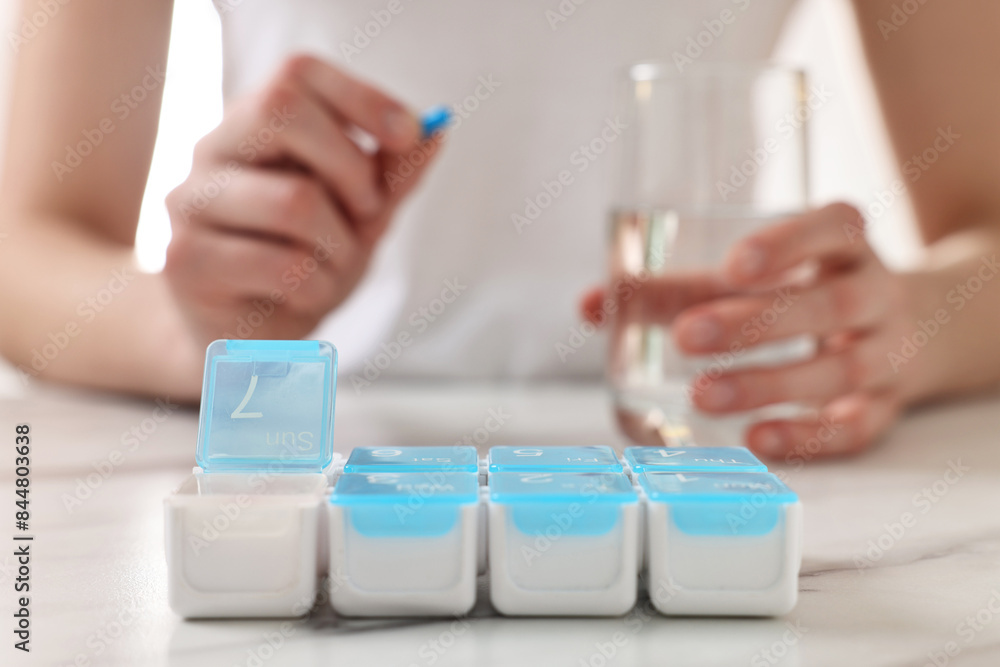 Woman with pills, organizer and glass of water at white marble table, selective focus Woman with pills, organizer and glass of water at white marble table, selective focus