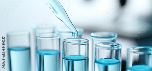 Tableau sur toile Dripping liquid from pipette into test tube on blurred background, closeup