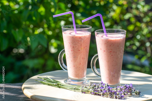 Glass of fresh strawberry milkshake, smoothie and fresh strawberries in garden on wooden table and green background. Healthy food and drink concept.