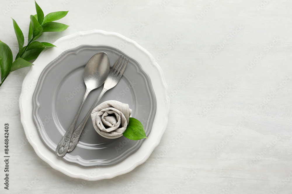 Stylish setting with cutlery, napkin, branch and plates on light textured table, top view. Space for text Stylish setting with cutlery, napkin, branch and plates on light textured table, top view. Space for text
