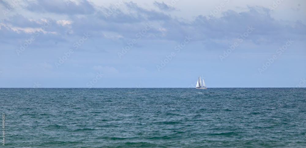 Sailboat sailing through the Atlantic Ocean near the coast, next to the horizon, on a summer day
