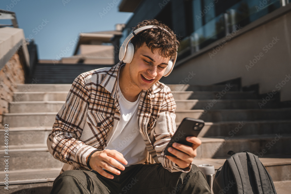 Young happy man sit on the stairs with headphones and listen music Young happy man sit on the stairs with headphones and listen music