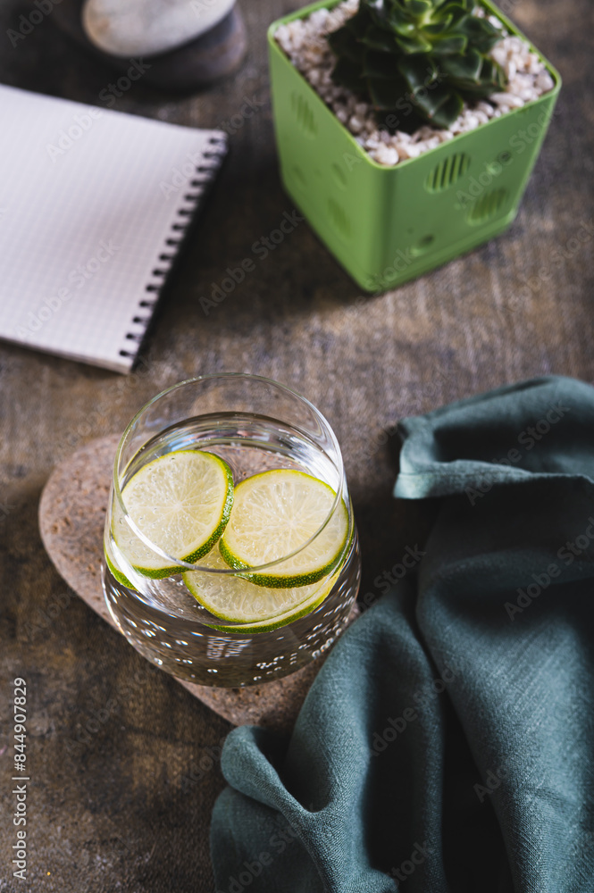 Clean water with lime slices in a glass on a stone, notepad and succulent on the table vertical view Clean water with lime slices in a glass on a stone, notepad and succulent on the table vertical view