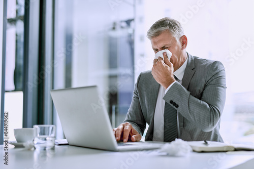 Blowing nose, tissue and businessman with laptop, desk and allergies or hayfever in office Sick or flu and computer for typing for mature male person, virus and influenza for infection with sneeze photo