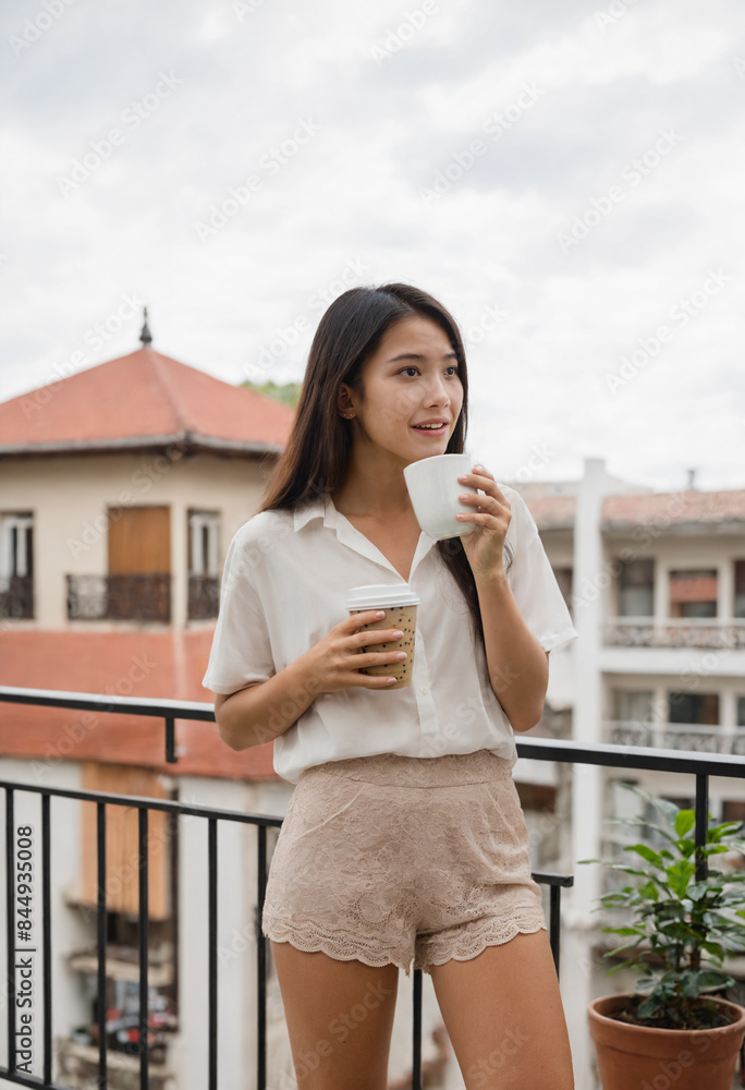 Young Asian woman with coffee, wearing shorts and white shirt, standing on balcony railing, home or office, weekend, relaxing, Japanese or Korean, age 18-30