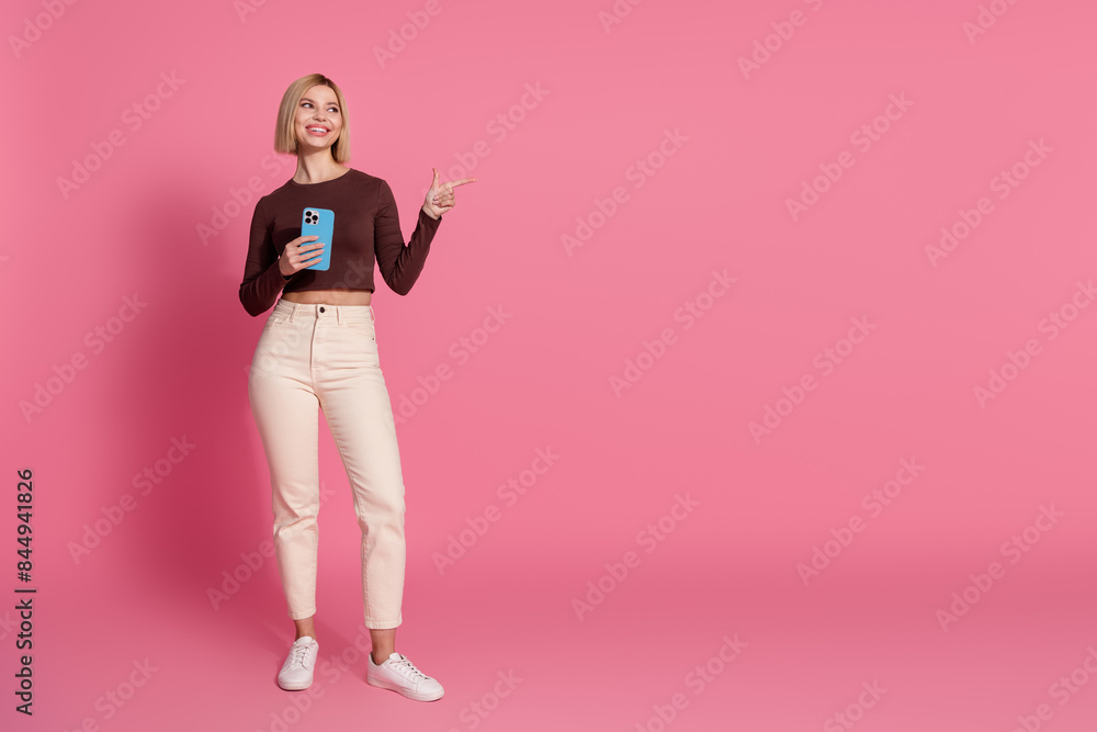 Full length photo of lovely young girl wear trendy clothes buy gadget look empty space isolated on pink color background Full length photo of lovely young girl wear trendy clothes buy gadget look empty space isolated on pink color background