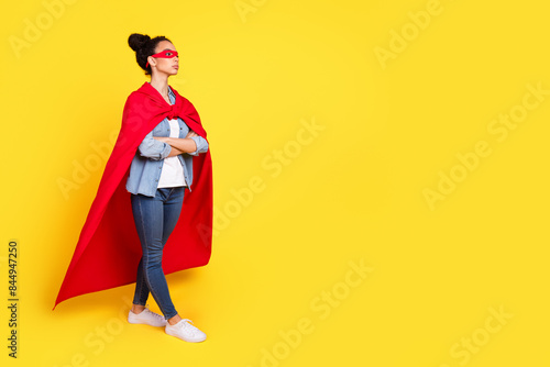 Full size photo of nice young girl crossed arms empty space superhero costume isolated on yellow color background