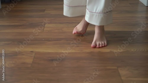 A person's feet on a wooden floor. Young woman barefoot circling and dancing in room. Female in white pants feet. Legs of unrecognizable girl.