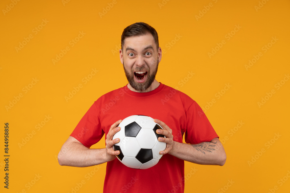 Studio portrait of amazed soccer fan man cheering for his favourite team while holding the ball in hands, isolated over bright colored orange yellow background Studio portrait of amazed soccer fan man cheering for his favourite team while holding the ball in hands, isolated over bright colored orange yellow background