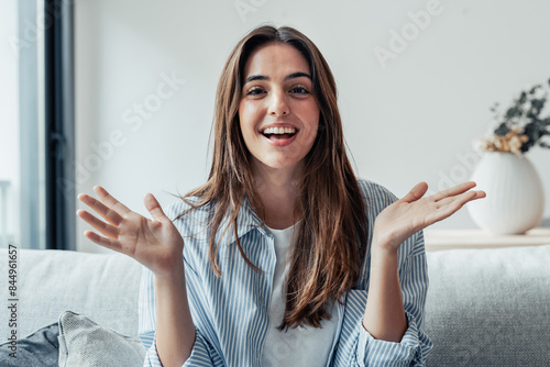 Head shot portrait smiling woman making video call to friends or relatives, using webcam, sitting on couch at home, happy young female blogger recording vlog, looking at camera, chatting online.