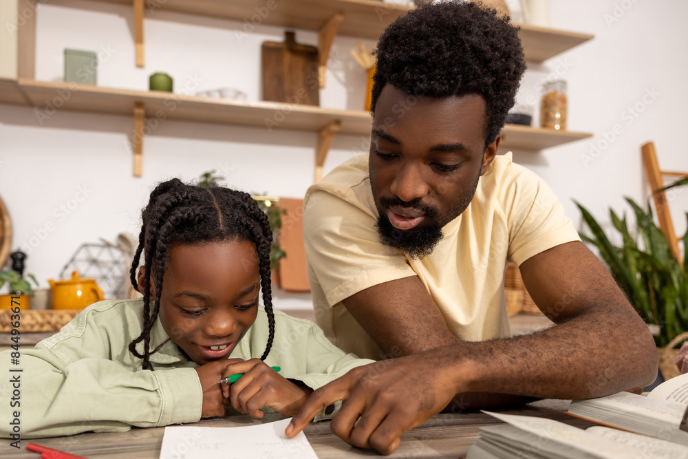 Naklejka premium Young multiethnic father helping his daughter with her homework
