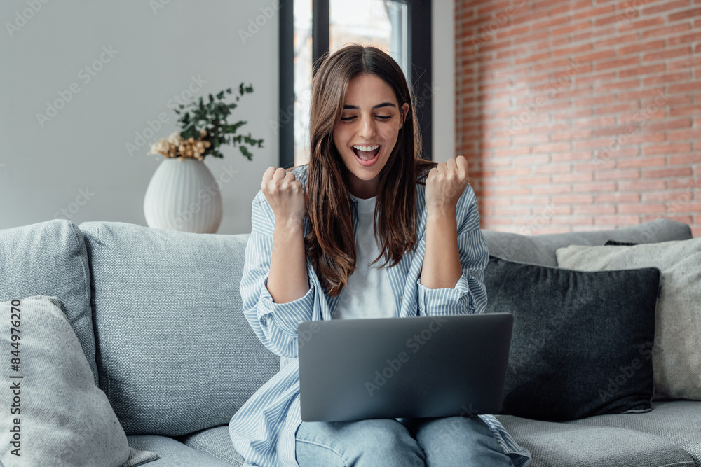Excited emotional screams with joy woman sit on sofa hold on lap notebook makes Yes hand gesture feels happy getting job of dream, e-mail sales discount special offer, on-line lottery victory concept. Excited emotional screams with joy woman sit on sofa hold on lap notebook makes Yes hand gesture feels happy getting job of dream, e-mail sales discount special offer, on-line lottery victory concept.
