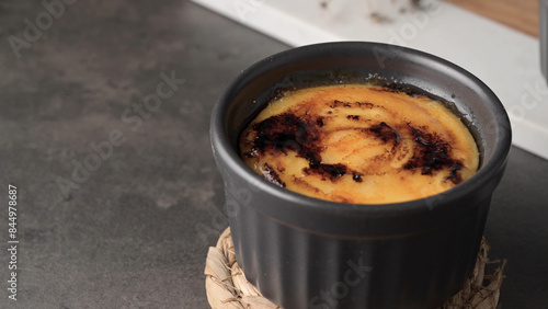 Obraz na plátně A close-up of a crème brûlée in a black ramekin on a woven coaster
