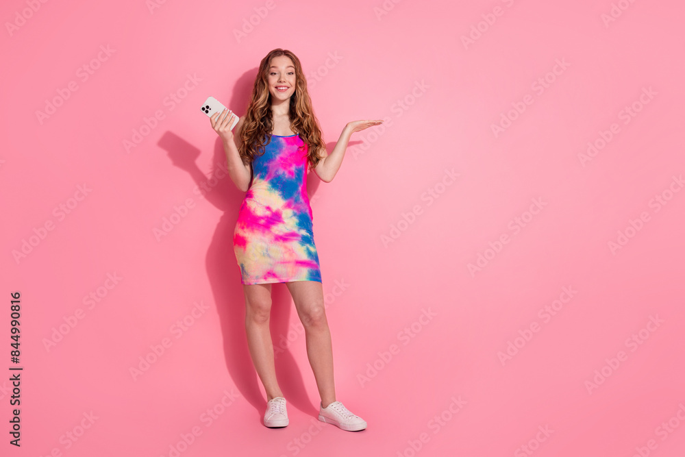Full length photo of charming positive girl wear retro outfit reading modern device arm empty space isolated pink color background Full length photo of charming positive girl wear retro outfit reading modern device arm empty space isolated pink color background