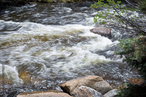 Close-up color photo of soft blurred de-focused water rushing down a mountain stream over large rocks and boulders on a warm summer day.