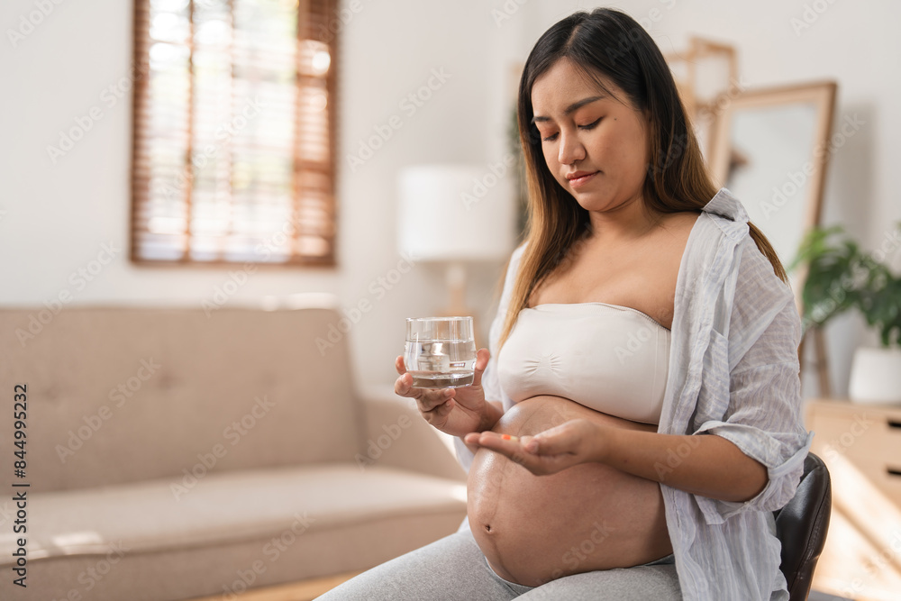 Pregnant Woman Sitting in a Modern Living Room, Holding a Glass of Water and Medication, Reflecting a Calm and Serene Atmosphere