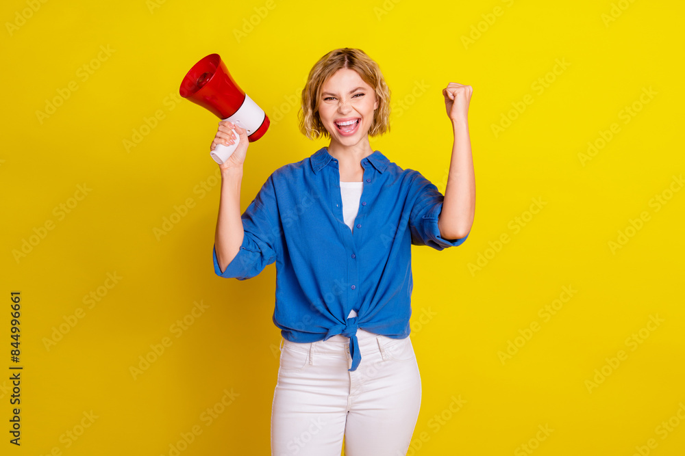 Portrait of pretty young lady loudspeaker raise fist wear blue shirt isolated on yellow color background Portrait of pretty young lady loudspeaker raise fist wear blue shirt isolated on yellow color background