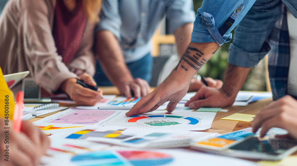 A collaborative work environment where a group of people are discussing and analyzing charts and graphs spread out on a table A collaborative work environment where a group of people are discussing and analyzing charts and graphs spread out on a table