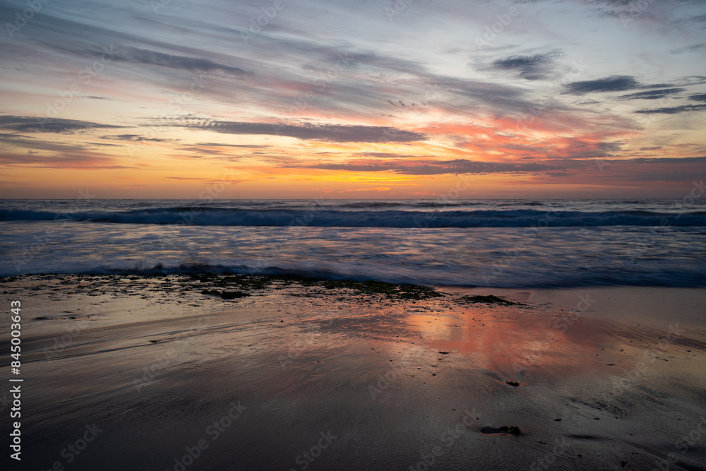 Fototapeta premium Sunrise over breaking waves beach orange yellow clouds