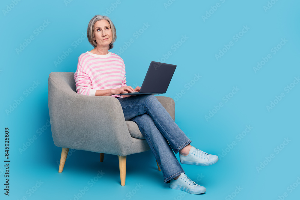 Full length photo of pensioner lady armchair netbook look skeptical empty space dressed striped garment isolated on blue color background Full length photo of pensioner lady armchair netbook look skeptical empty space dressed striped garment isolated on blue color background