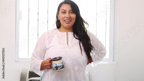 Beautiful middle-aged Latina woman holding cup of Mexican coffee and talking in front of the camera