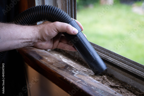 Cleaning debris out of window ledge and grooves with vacuum.
