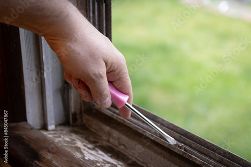Cleaning debris out of window ledge and grooves with screwdriver tool.