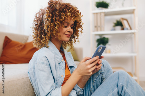Cozy Living: Young Woman Holding Phone and Smiling while Relaxing on Sofa in her Home