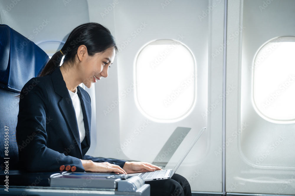 A woman in a formal suit sits in a window seat of an economy class section, looking out the airplane window, ready for her business journey. A woman in a formal suit sits in a window seat of an economy class section, looking out the airplane window, ready for her business journey.