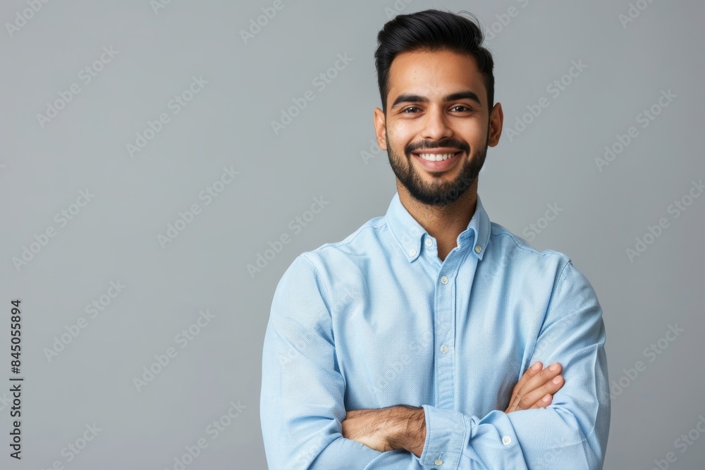 A man with a beard smiles while standing with his arms crossed in front of a grey background A man with a beard smiles while standing with his arms crossed in front of a grey background