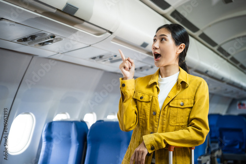 A young Asian woman, an airplane passenger, sits by the window seat, studying abroad. She gazes out the window, ready for takeoff in the economy class section.
