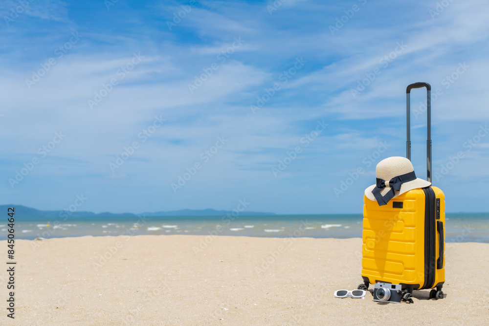 Naklejka premium Suitcase with beach accessories on sand, hat, sunglasses, camera, sea and sky background. summer travel concept.