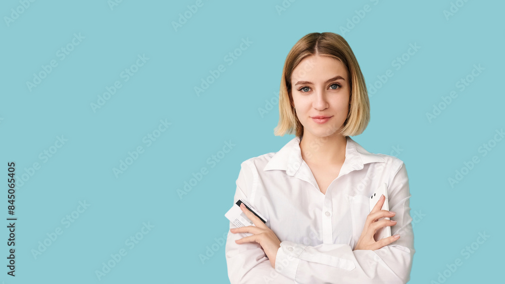 Mobile banking. Business account. Commercial promo. Satisfied woman arms crossed holding phone and credit card isolated on blue empty space. Mobile banking. Business account. Commercial promo. Satisfied woman arms crossed holding phone and credit card isolated on blue empty space.