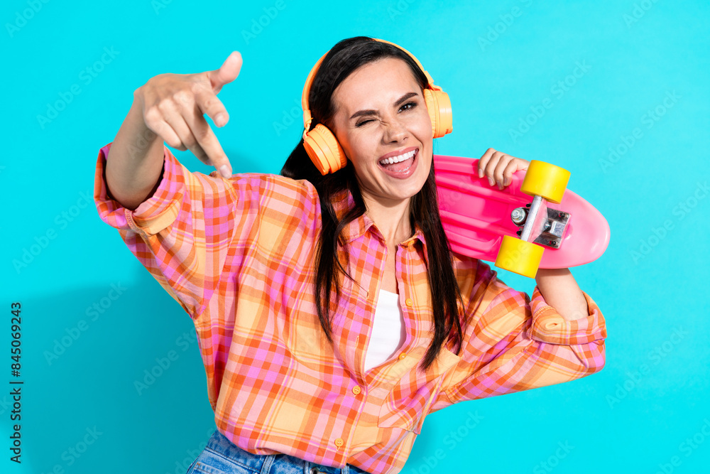 Photo portrait of lovely young lady headphones hold skateboard dressed stylish plaid garment isolated on aquamarine color background Photo portrait of lovely young lady headphones hold skateboard dressed stylish plaid garment isolated on aquamarine color background