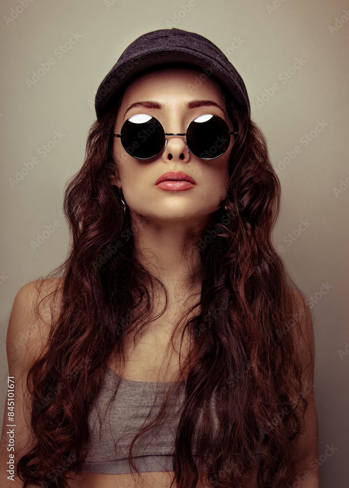 Beautiful brunette woman in fashion sun glasses and cap with long brown curly hair style posing in studio. Closeup. Beautiful brunette woman in fashion sun glasses and cap with long brown curly hair style posing in studio. Closeup.