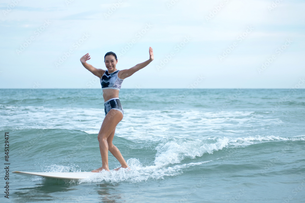 Asian surfing woman riding the waves on sunny day, outdoor activities, water sports activities concept