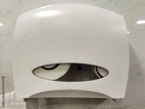 A double roll plastic toilet tissue dispenser mounted on a white wall holds two rolls neatly. The sleek, translucent window reveals the tissue inside, ensuring cleanliness in a modern bathroom.
