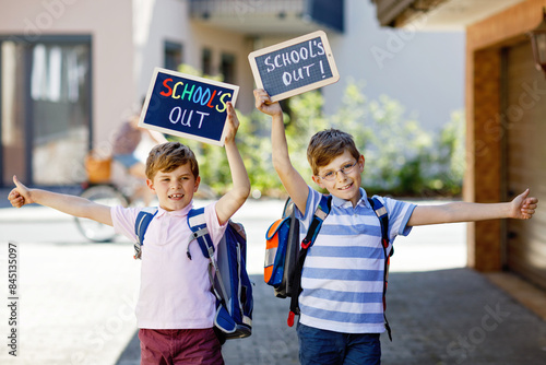 Two little kid boys with backpack or satchel. Schoolkids on the way to school. Healthy children, brothers and best friends outdoors on street leaving home. School's out on chalk desk. Happy siblings. photo
