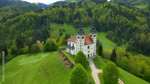 Church of St. Volbenka On Hilltop Overlooking Lush Scenery In Na Logu, Slovenia. ascending drone, tilt-down shot photo