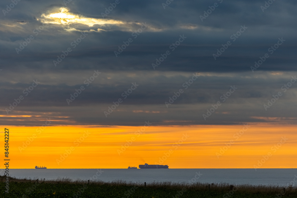 A breathtaking sunset views ships on the distant ocean horizon amidst a dramatic sky filled with clouds A breathtaking sunset views ships on the distant ocean horizon amidst a dramatic sky filled with clouds