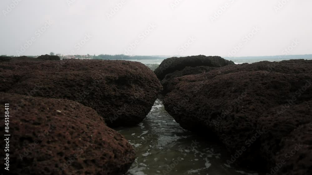 Ocean waves gently splash between rugged red rocks under an overcast sky Ocean waves gently splash between rugged red rocks under an overcast sky
