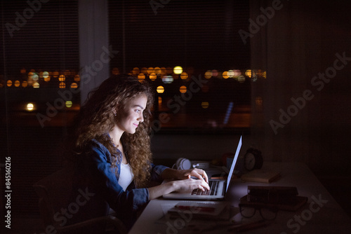 Cuadro en lienzo Beautiful university student is writing her thesis on a laptop at night, sitting at home at table, focusing on her research