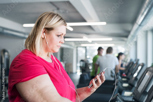 Overweight woman exercising on treadmill in gym, listening music. photo