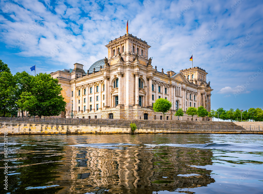 Fototapeta premium Reichstagsgebäude in Berlin, im Vordergrund die Spree, leicht bewölkter blauer Himmel, horizontal